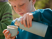 Close up of young boy pouring water from insulated flask\n