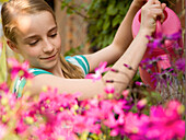 Portrait eines jungen Mädchens beim Blumengießen mit rosa Gießkanne
