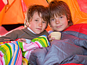 Portrait of two boys sitting in a tent in sleeping bags\n