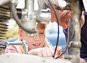 Young girl helping grandfather repairing motorbike engine\n