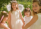 Young girls in fancy dress holding hands in a garden\n