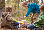 Three boys around campfire boiling water in a kettle\n