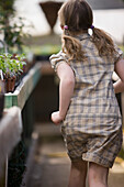 Back of young girl running around inside a nursery greenhouse\n
