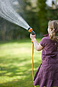 Back of young girl spraying the lawn with garden hose\n