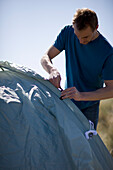 Portrait eines jungen Mannes, der steht und sein Zelt aufbaut