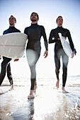 Drei Surfer laufen mit Surfbrettern in der Hand aus dem Meer