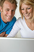 Close up of a young couple laughing and looking at laptop computer screen\n