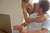 Young couple in front of laptop computer embracing and looking at each other\n