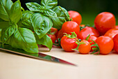 Close up of cherry tomatoes basil leaves and a knife blade\n
