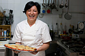 Woman chef holding a tray of stuffed tomatoes and smiling\n