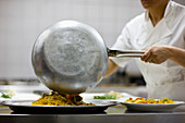 Woman chef holding a frying pan and preparing seafood pasta for service\n