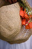 Extreme close up of a straw hat with red poppies and camomile flowers\n