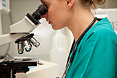 Lab technician looking into microscope\n