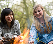 Two smiling teenaged girls roasting marshmallow over a campfire\n