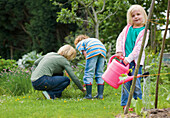 Young blonde girl standing and watering plants with pink watering can\n