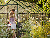Back view of man and young girl tending plants in a greenhouse\n