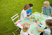 Children sitting and painting in the garden\n