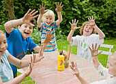 Children smiling and laughing with their arms up and hands covered in paint\n