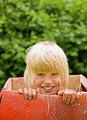 Close up of a young blonde boy in a cardboard box smiling\n