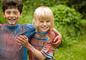 Two young boys covered in watercolor paint laughing in a garden\n
