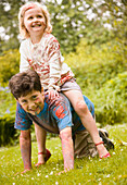 Young girl riding piggyback on young boy both dirty with watercolor paint\n