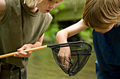 Two young boys inspecting  the content of a fishing net\n
