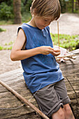 Junge knüpft einen Knoten mit einer Schnur um einen Stein