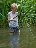 Young boy fishing in a river with his legs in the water\n