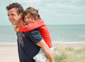 Young boy riding piggyback on his father shoulder on a beach\n