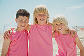 Drei lächelnde Jungen am Strand mit identischen rosa T-Shirts
