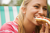 Close up of a teenaged girl eating a hot dog\n