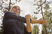 Young woman standing in a forest stretching her arm\n