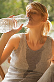 Nahaufnahme einer jungen Frau, die mit geschlossenen Augen Wasser aus einer Flasche trinkt
