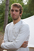 Young man standing by a tent with his arms crossed\n