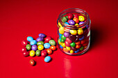 Still life multicolored candy in glass jar on red background\n
