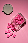 Rosafarbene Bonbonherzen, die aus einem Glasgefäß auf rosafarbenem Hintergrund quellen