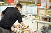 Rear view of man in supermarket working at deli counter\n