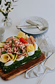 Swedish sandwich cake with shrimps, cheese, ham and eggs on wooden board at table\n