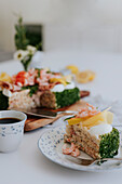 Schwedischer Sandwichkuchen mit Krabben, Käse, Schinken und Eiern auf einem Teller am Tisch