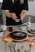 Woman putting powdered sugar on freshly baked chocolate cake\n