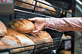 Close-up of man picking bread in bakery section of supermarket\n