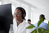 Mittlere erwachsene Frau benutzt Headset während sie im Büro sitzt