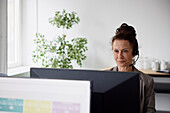 Lächelnde reife Geschäftsfrau, die ein Headset im Büro vor einem Computerbildschirm benutzt