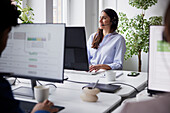 Lächelnde mittlere erwachsene Geschäftsfrau, die ein Headset im Büro vor einem Computerbildschirm benutzt