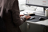 Mittelteil einer Frau im Büro bei der Nutzung eines Desktop-PCs
