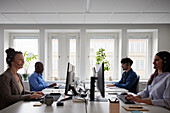 Männer und Frauen arbeiten im Büro, benutzen PC-Desktops und unterhalten sich über Headset