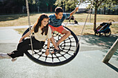 Siblings having fun swinging on swing on playground\n