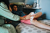 Caring mother putting ice pack on son's injured foot\n