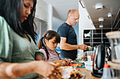 Family with daughter preparing meal together at home\n