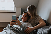 Weibliches Paar liegt auf dem Sofa und schaut auf das Handy